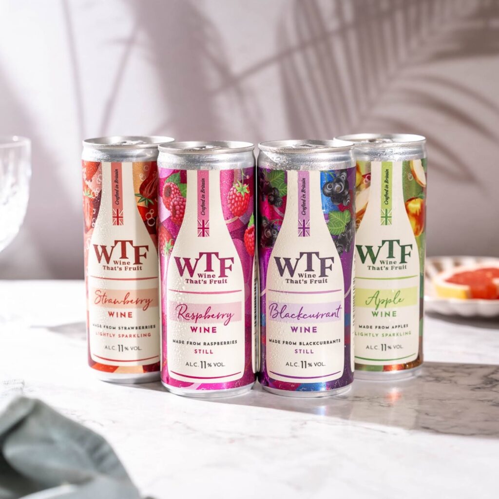 Four cans featuring Wine That's Fruit's strawberry, raspberry, blackcurrant and apple wines standing on a table.